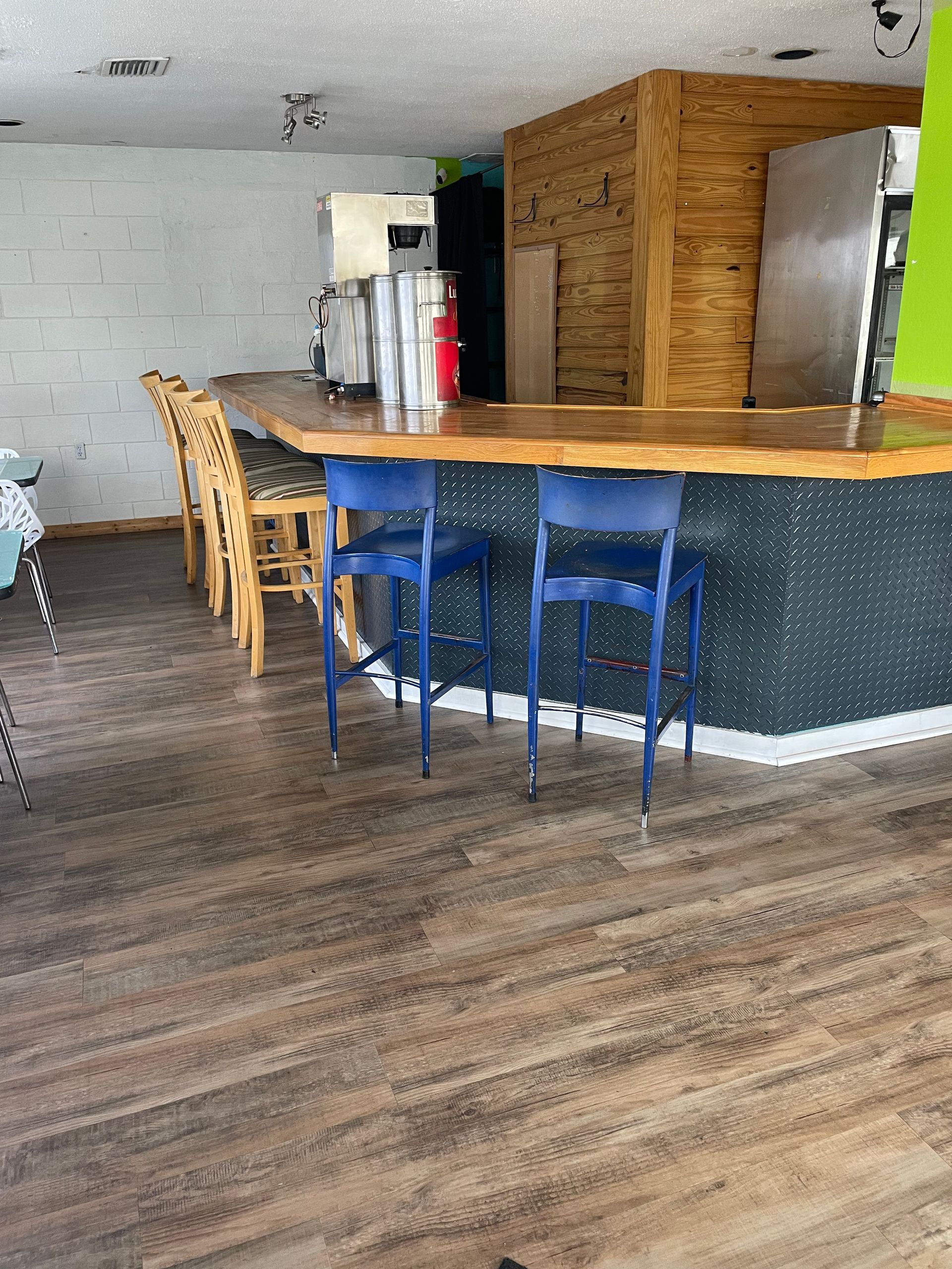 Empty bar with blue stools, wooden counter, and wood-paneled back wall in a rustic interior.