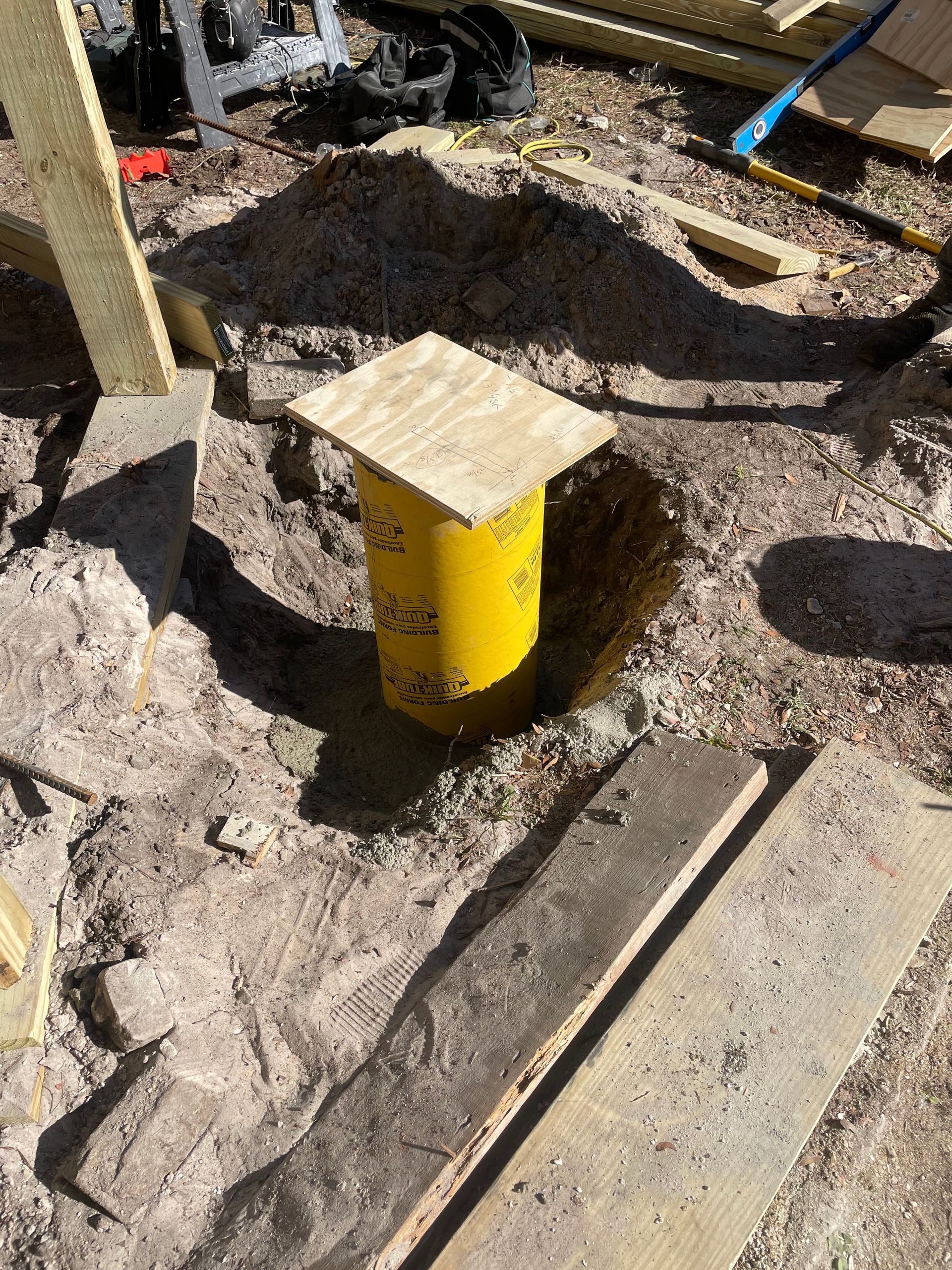 Yellow utility pipe with a wooden cap set in a rough dirt and concrete worksite