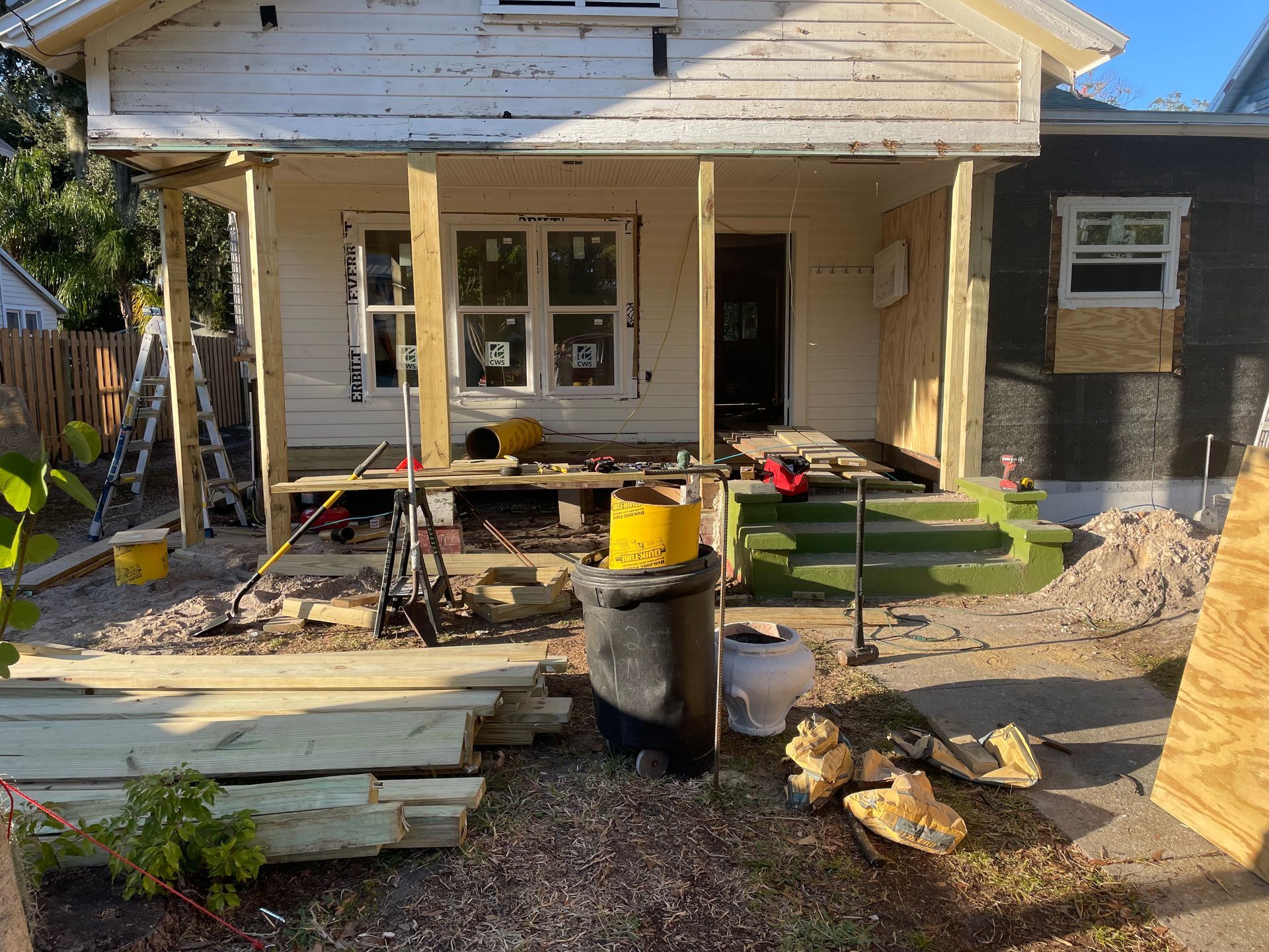 Front porch under construction with tools, lumber, and debris in a yard.