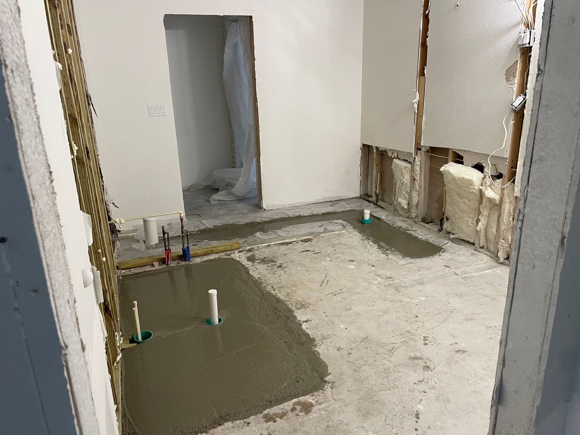 Partially renovated room with exposed walls, floor tools, and fresh concrete patches