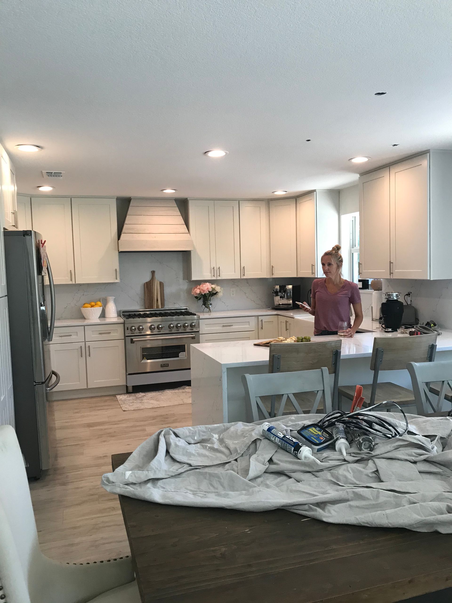 Bright kitchen with white cabinets and island; a person stands by the counter amid renovation clutter.