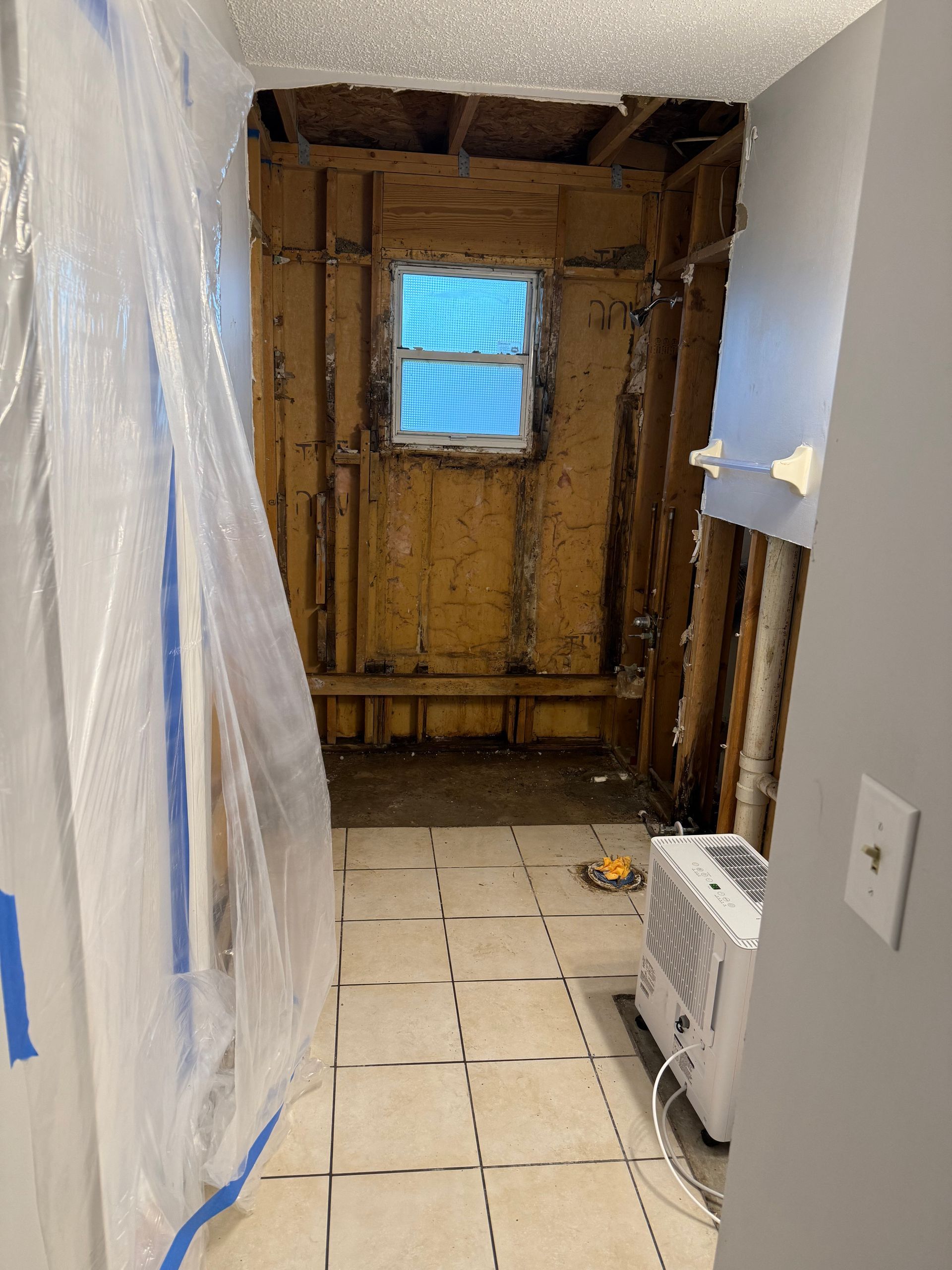 Partially renovated room with exposed wall studs, plastic sheeting, and a small window at the back
