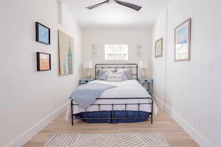 Bright minimalist bedroom with a black metal bed, blue bedding, wall art, and a ceiling fan