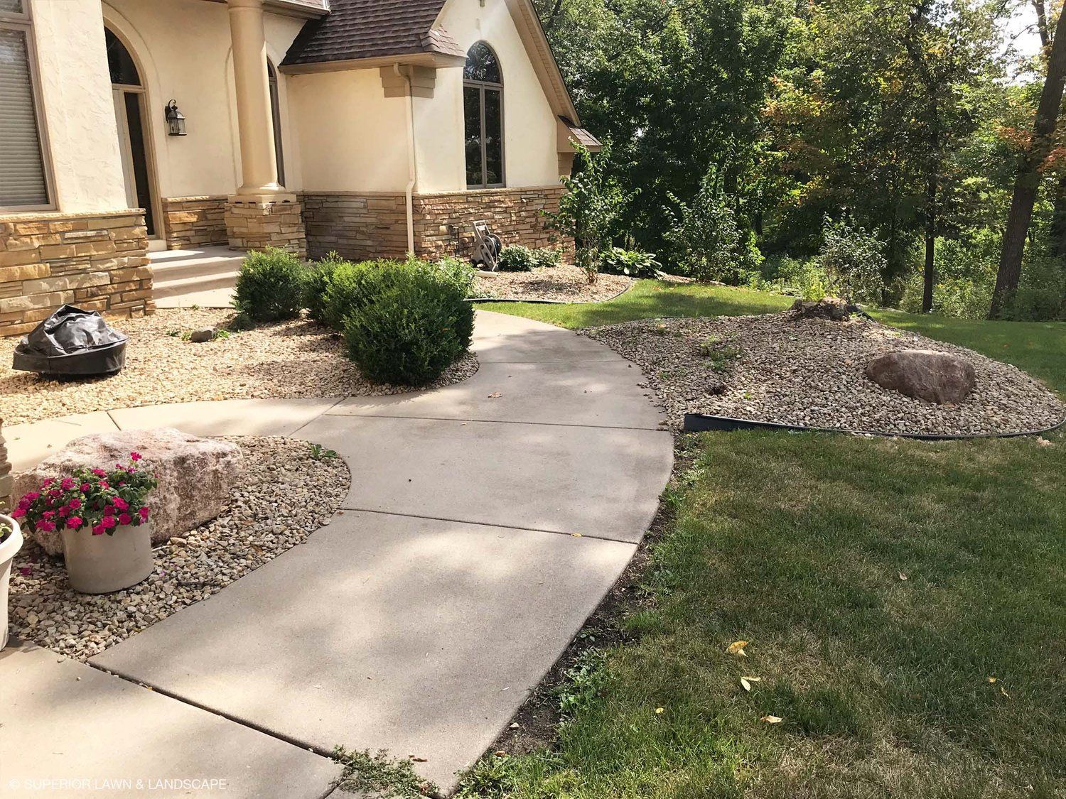 A concrete walkway leading to a house with flowers in front of it.