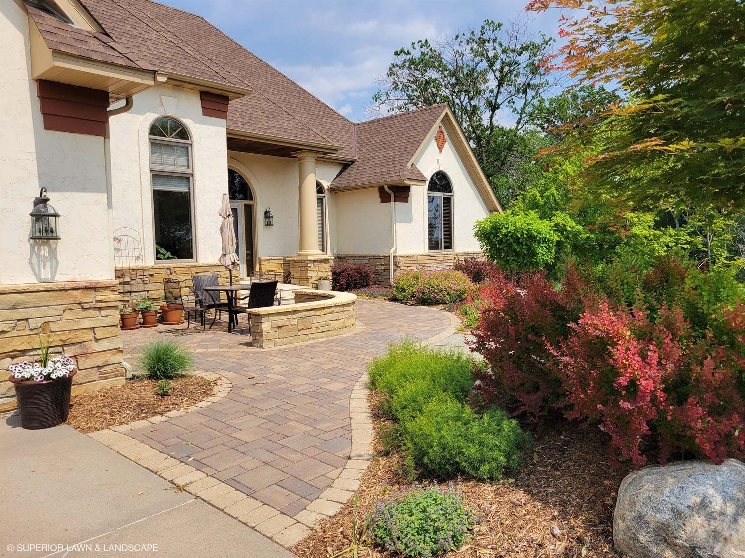 A large white house with a patio in front of it surrounded by trees and bushes.