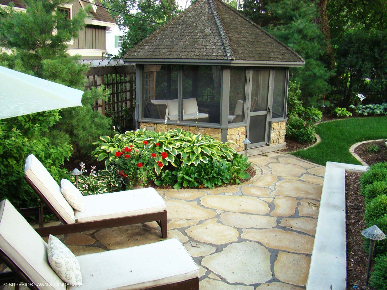 A screened in gazebo sits in the middle of a garden