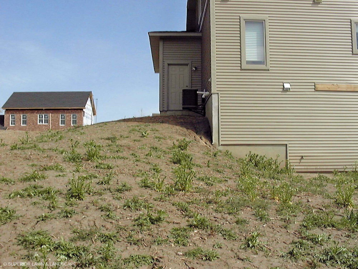 A house sits on top of a grassy hill next to another house