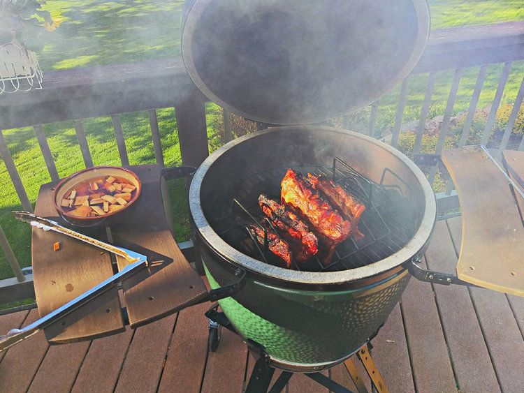 Ribs are cooking on a grill on a wooden deck.