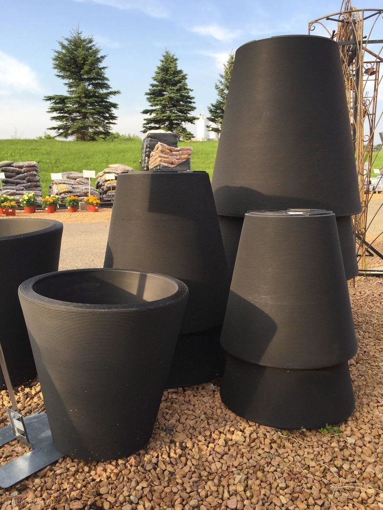 A bunch of black pots are stacked on top of each other on gravel.
