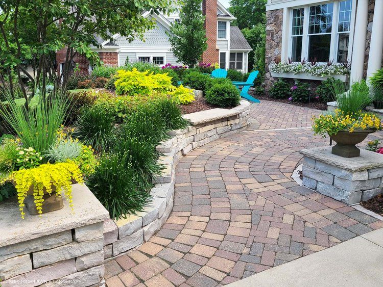 A brick walkway leading to a house with a blue chair in the background.