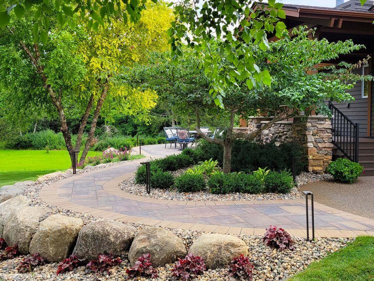 A stone walkway leading to a house surrounded by trees and rocks.