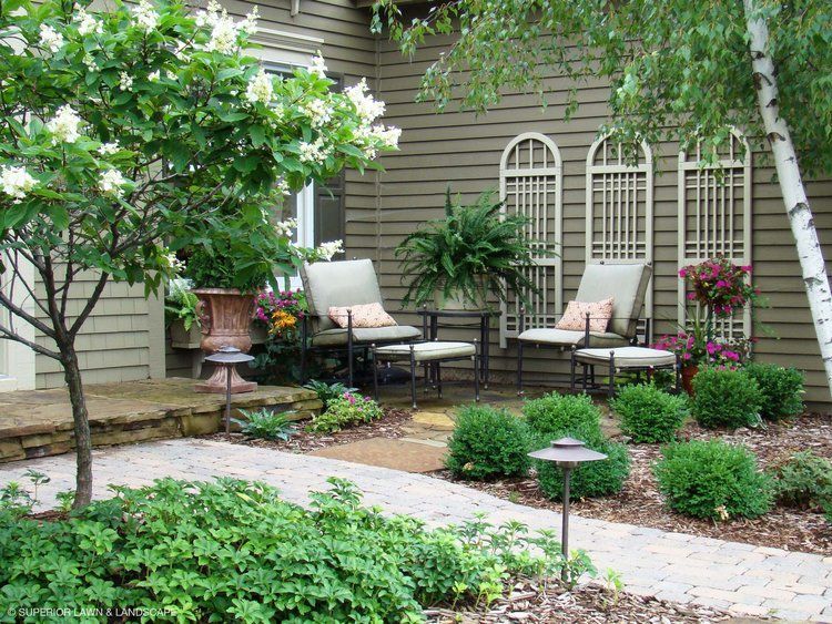 A patio with chairs and a tree in front of a house.