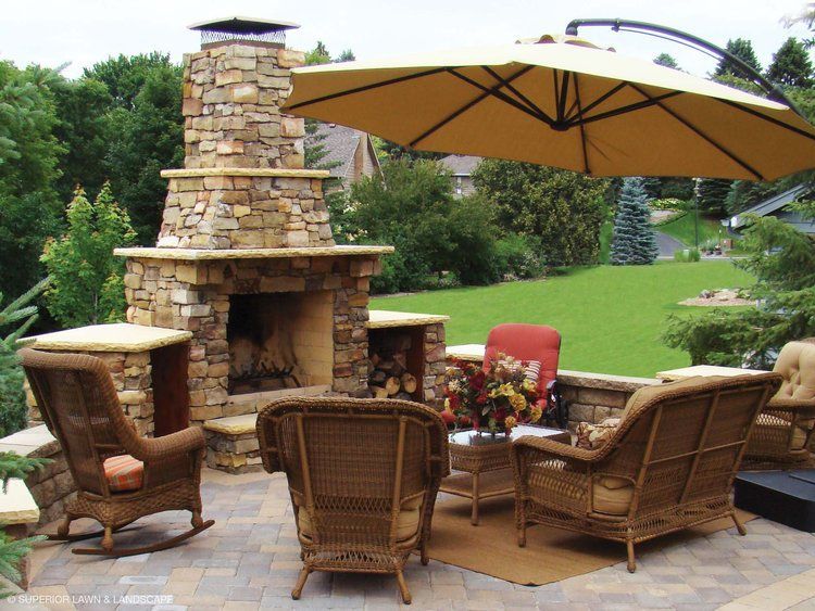 A patio with rocking chairs a fireplace and an umbrella