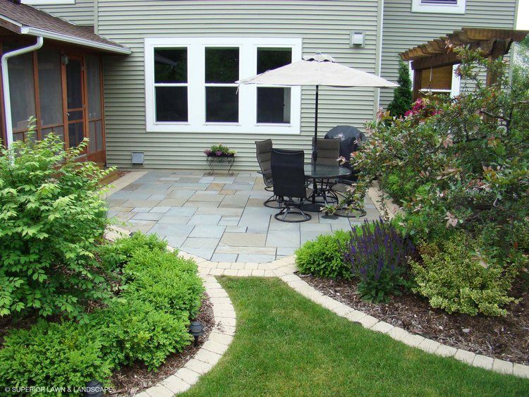 A patio with a table and chairs and an umbrella in front of a house