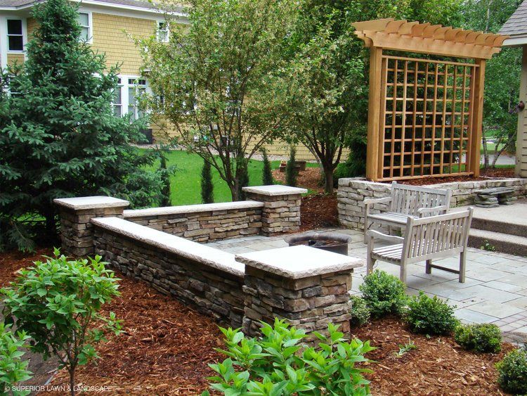 A stone wall surrounds a fire pit in a backyard.