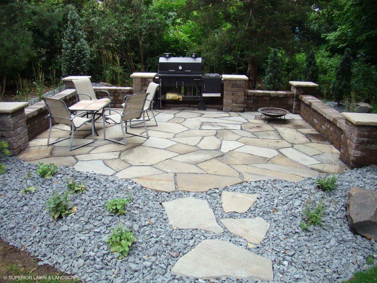A stone patio with a grill and chairs