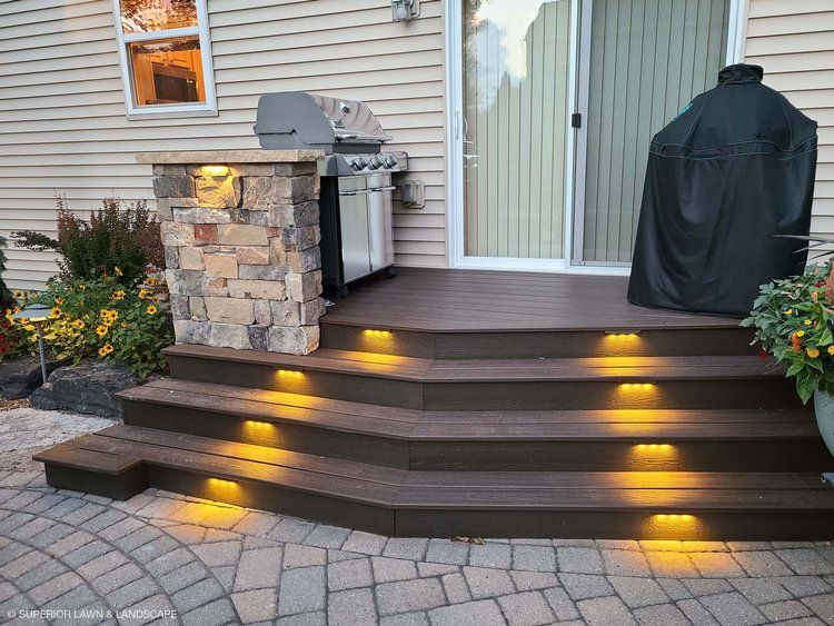 A wooden deck with stairs leading up to it and a grill.