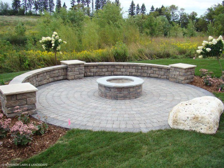 A fire pit is surrounded by a stone wall in the middle of a lush green field.