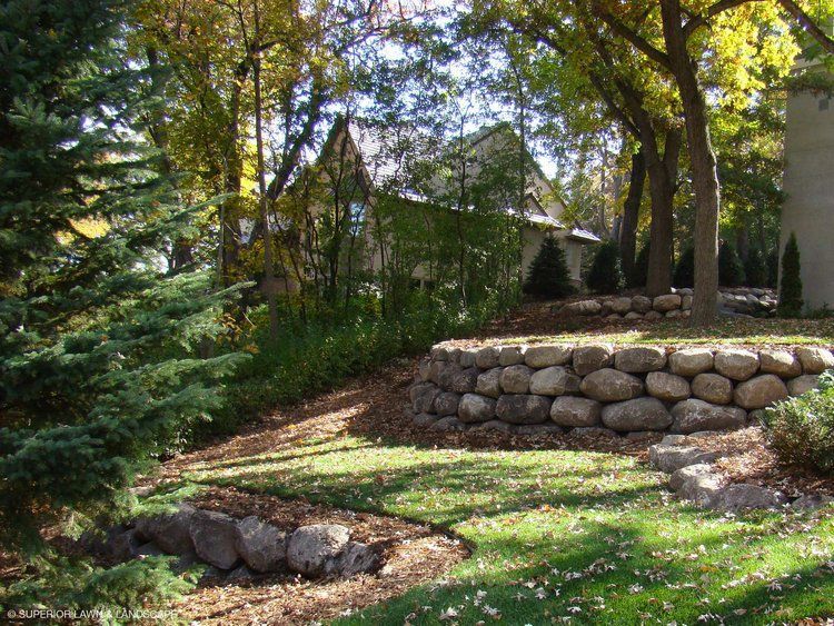 A stone wall surrounds a lush green lawn in front of a house.