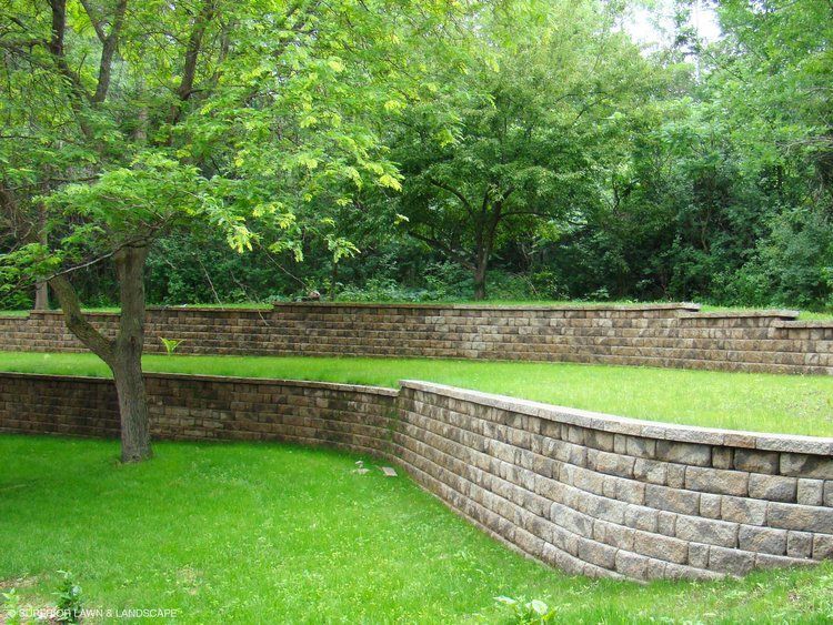 A brick wall surrounds a lush green lawn with trees in the background.