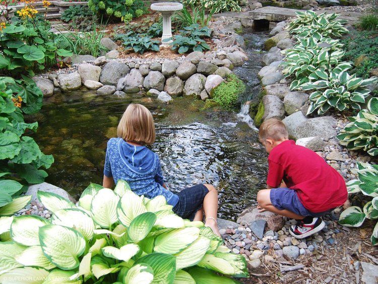 A boy and a girl are looking at a stream in a garden.