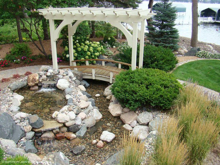 A garden with a pergola and a bridge over a pond