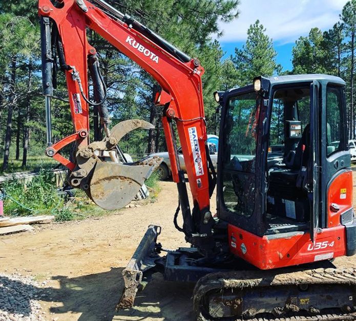 Red Kubota L35-4 excavator on a dirt road, arm raised. Dark cab, metal tracks, outdoors.