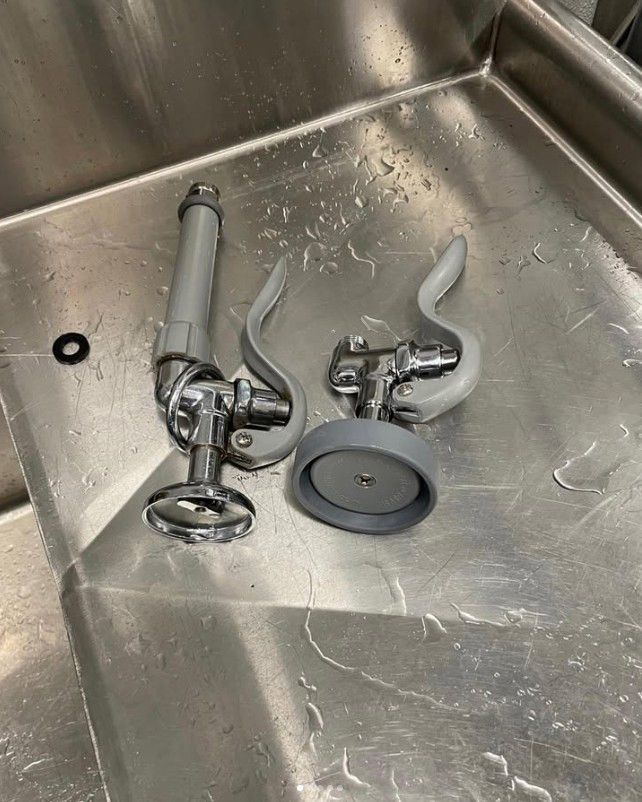 Two commercial kitchen spray valves on a stainless steel sink.