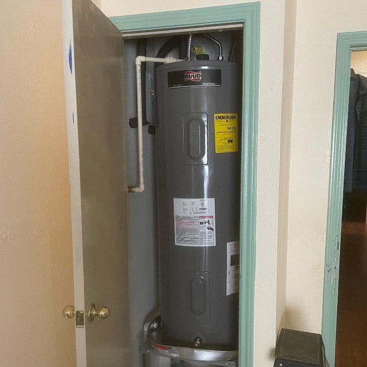 A tall, gray water heater is housed in a closet with open door. A pale yellow wall and green trim are visible.