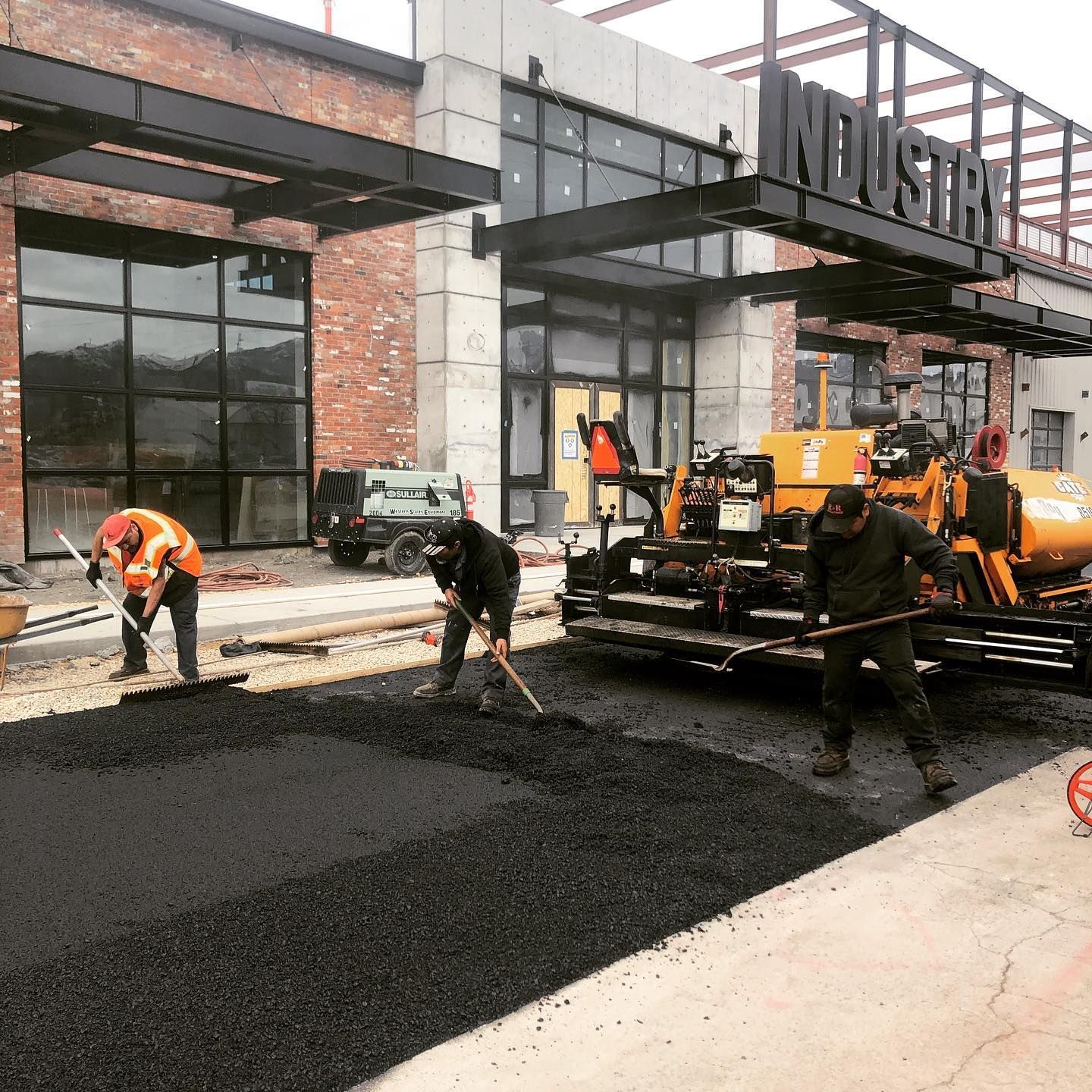 a group of construction workers are working on a road in front of an industrial building