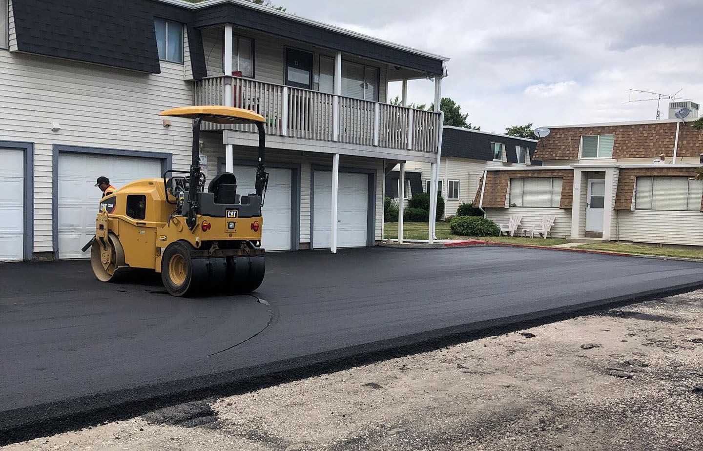 a yellow roller is laying asphalt in front of a house