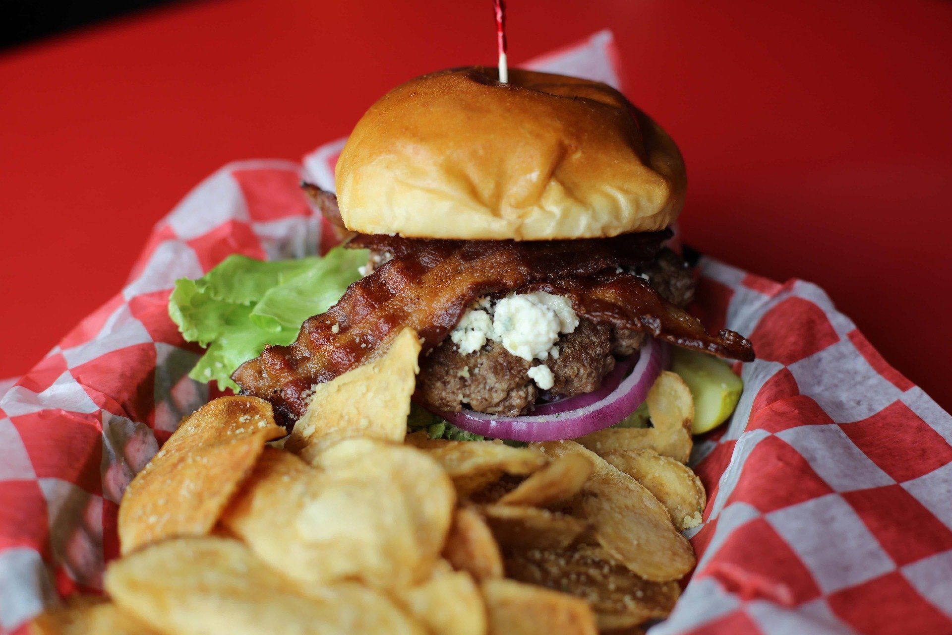 A hamburger and chips are on a checkered paper on a table.