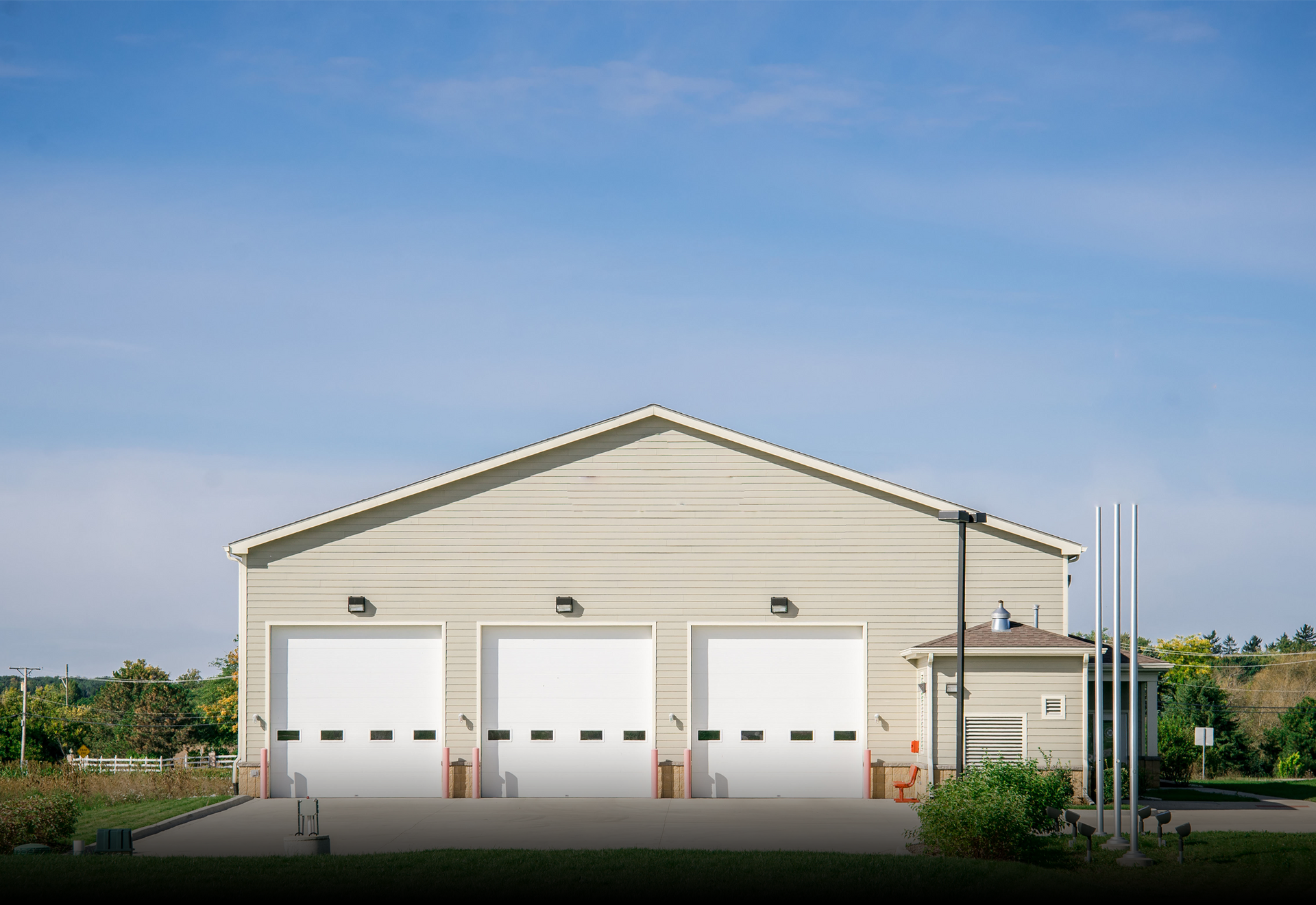 A large building with three white garage doors and a blue sky in the background