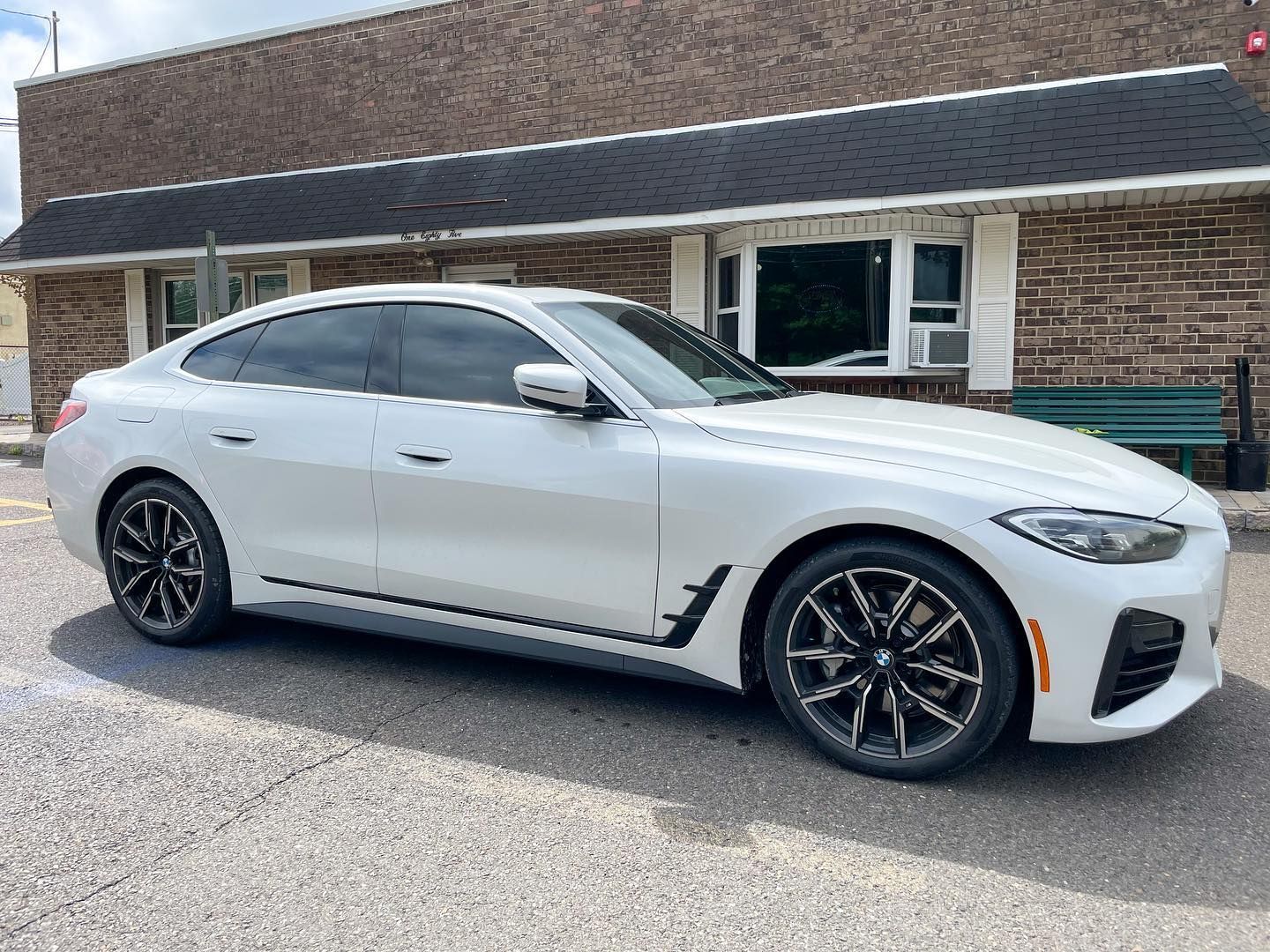 White BMW sedan parked in front of a brick building. Black rims and tinted windows.