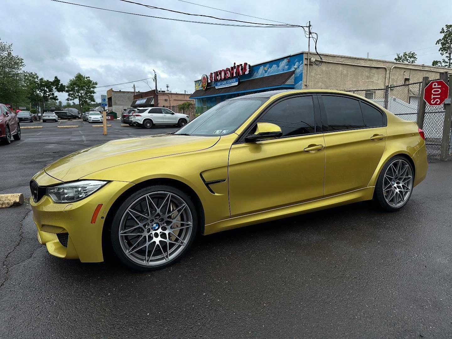 Yellow BMW sports car parked on wet asphalt in front of a storefront on a cloudy day.