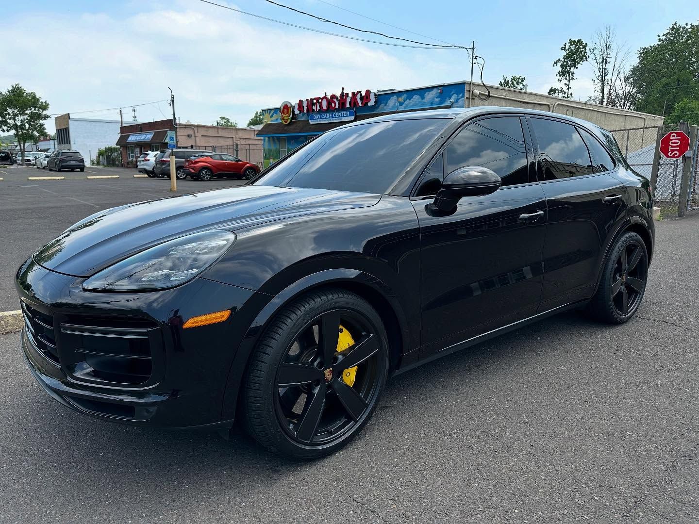 Black Porsche Cayenne SUV with black wheels and yellow brake calipers parked on asphalt.