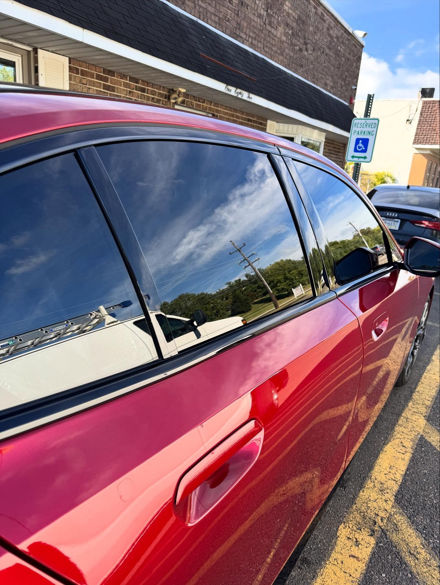 Red car parked next to a building, windows reflecting the sky.