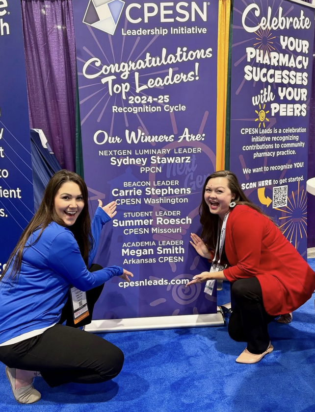 Two women pointing to a banner listing award recipients at a CPESN leadership event; purple and blue color scheme.
