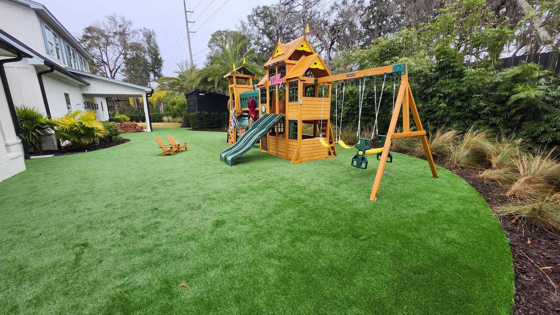 A playground set is sitting on top of a lush green lawn in front of a house.