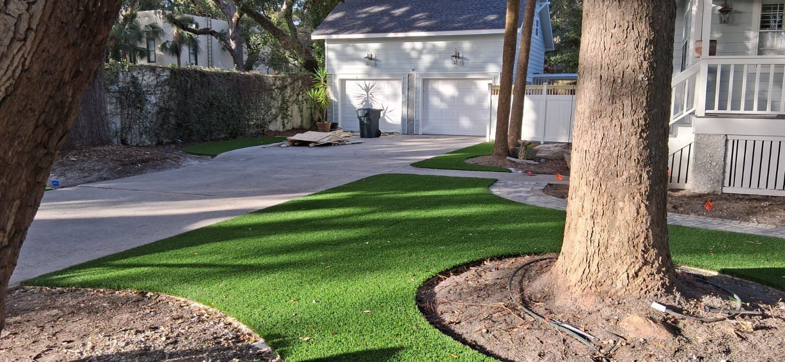 A lawn with a tree in the middle of it and a house in the background.