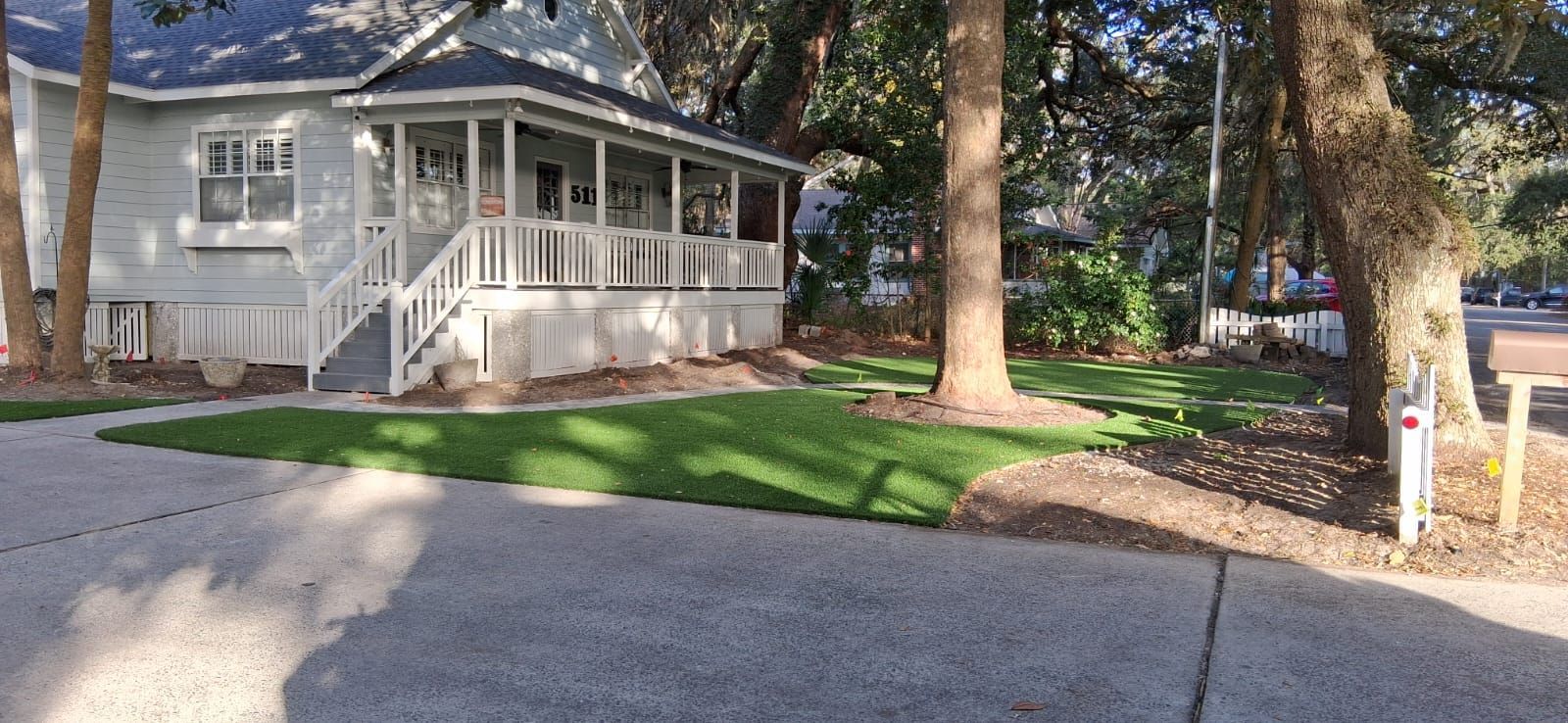 A white house with a porch is surrounded by trees and grass.