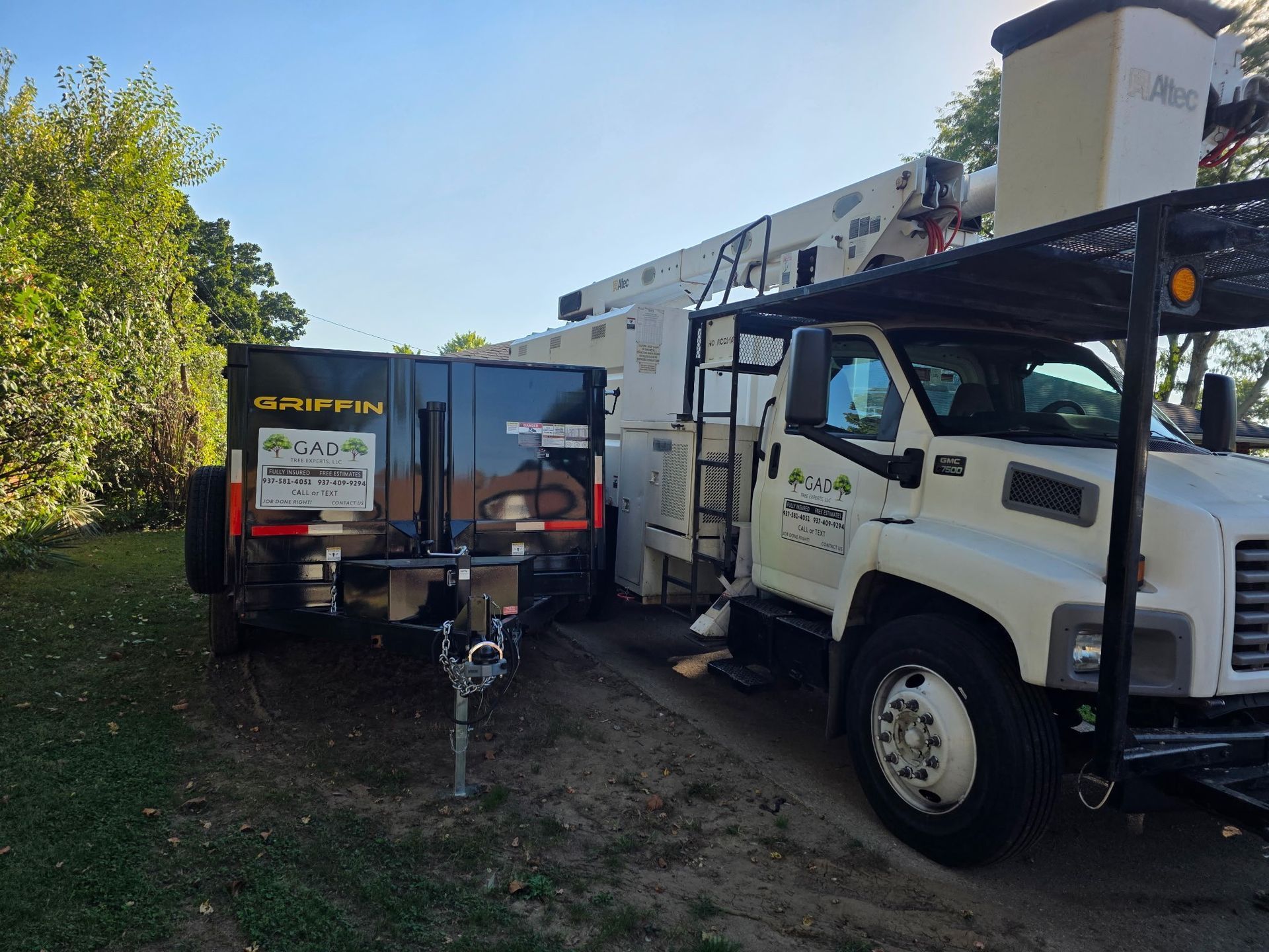 Tree service truck with trailer parked on grass near a tree.