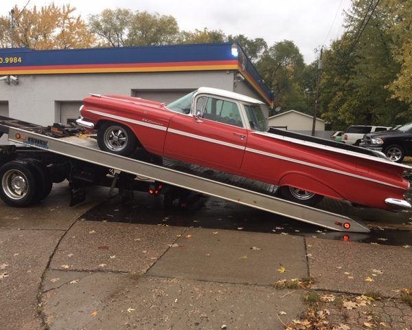 A red 1959 Chevrolet El Camino being loaded onto a flatbed tow truck in an outdoor setting.