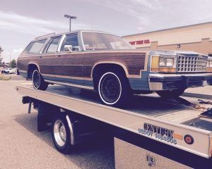 A classic wood-paneled station wagon loaded on a flatbed tow truck in a parking lot.