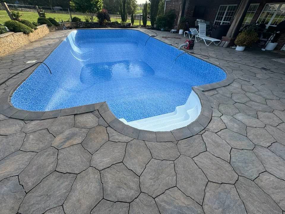 Rectangular in-ground pool with blue tile. Stone patio surrounds pool, steps at one end. Exterior setting.