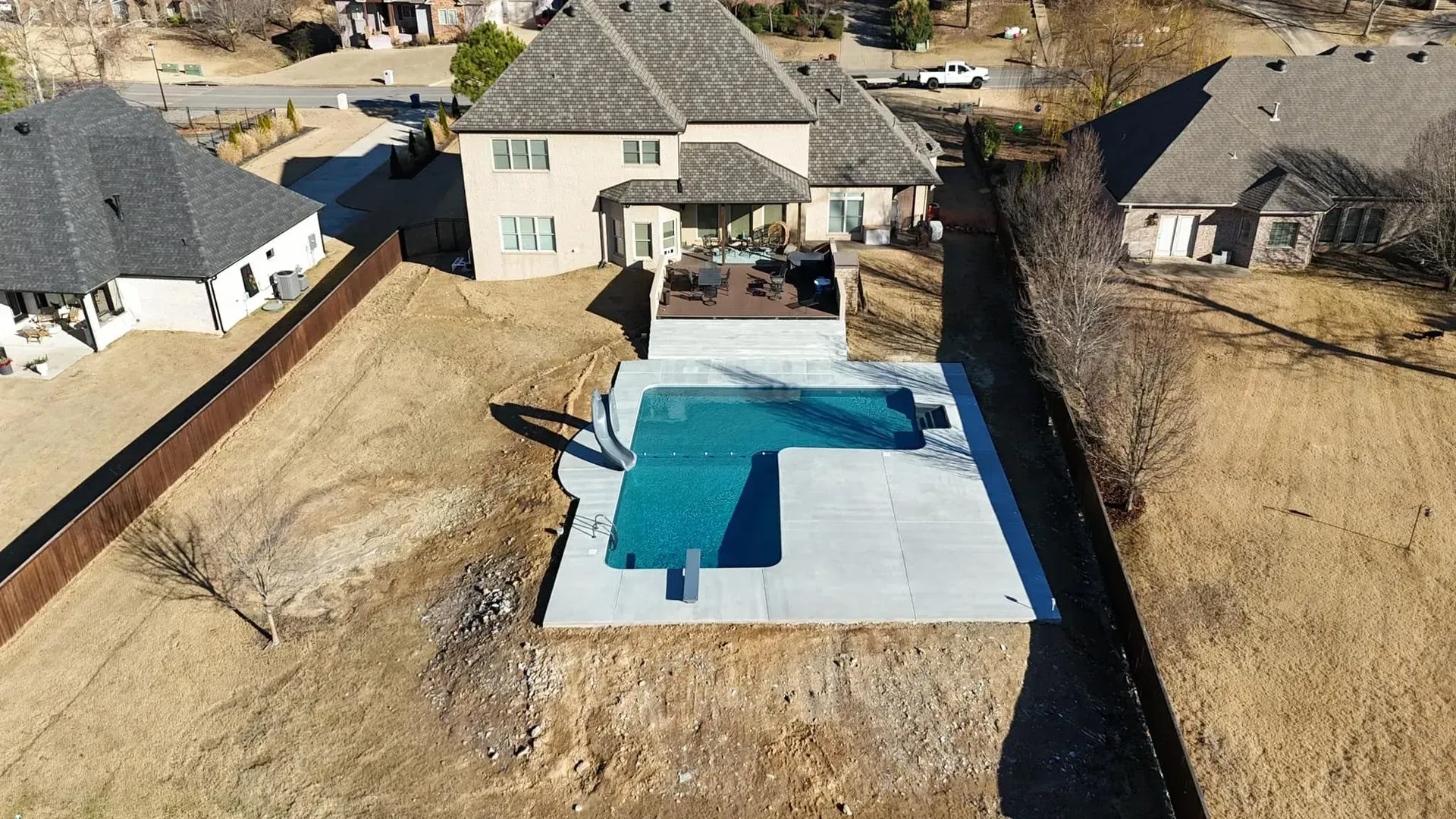 An aerial view of a two-story beige house with a pool and patio in the backyard.