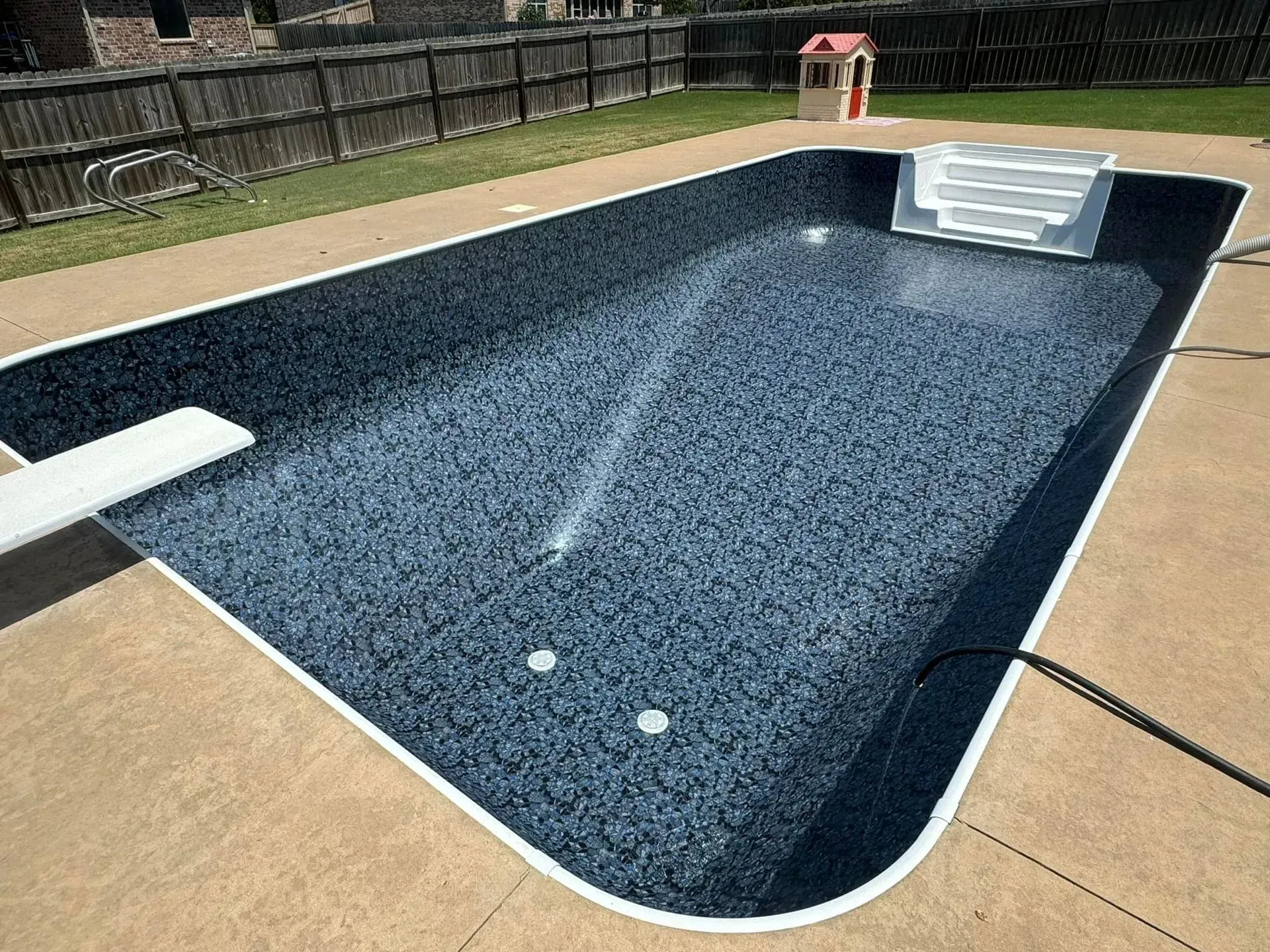 Empty rectangular swimming pool with blue speckled interior, white diving board and steps. Concrete patio surrounds.