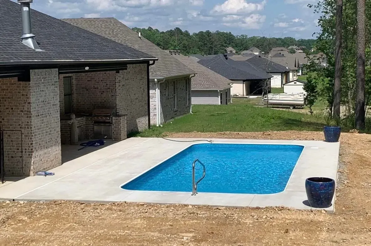 Backyard pool with patio, blue water, next to a house with brick columns and blue planters.