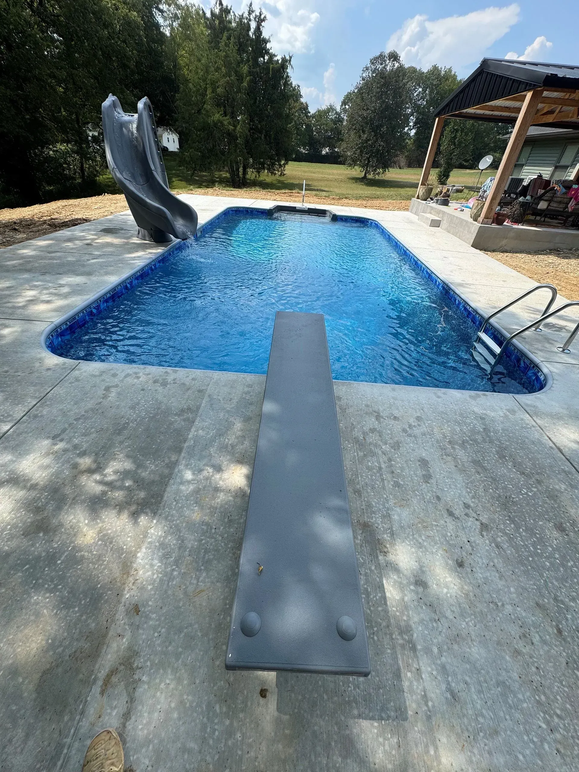 Swimming pool with a diving board and a slide, surrounded by concrete. Blue water.