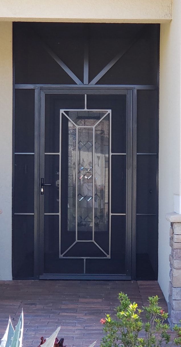 Dark gray security door with decorative glass panel, surrounded by black screen. Brick walkway.